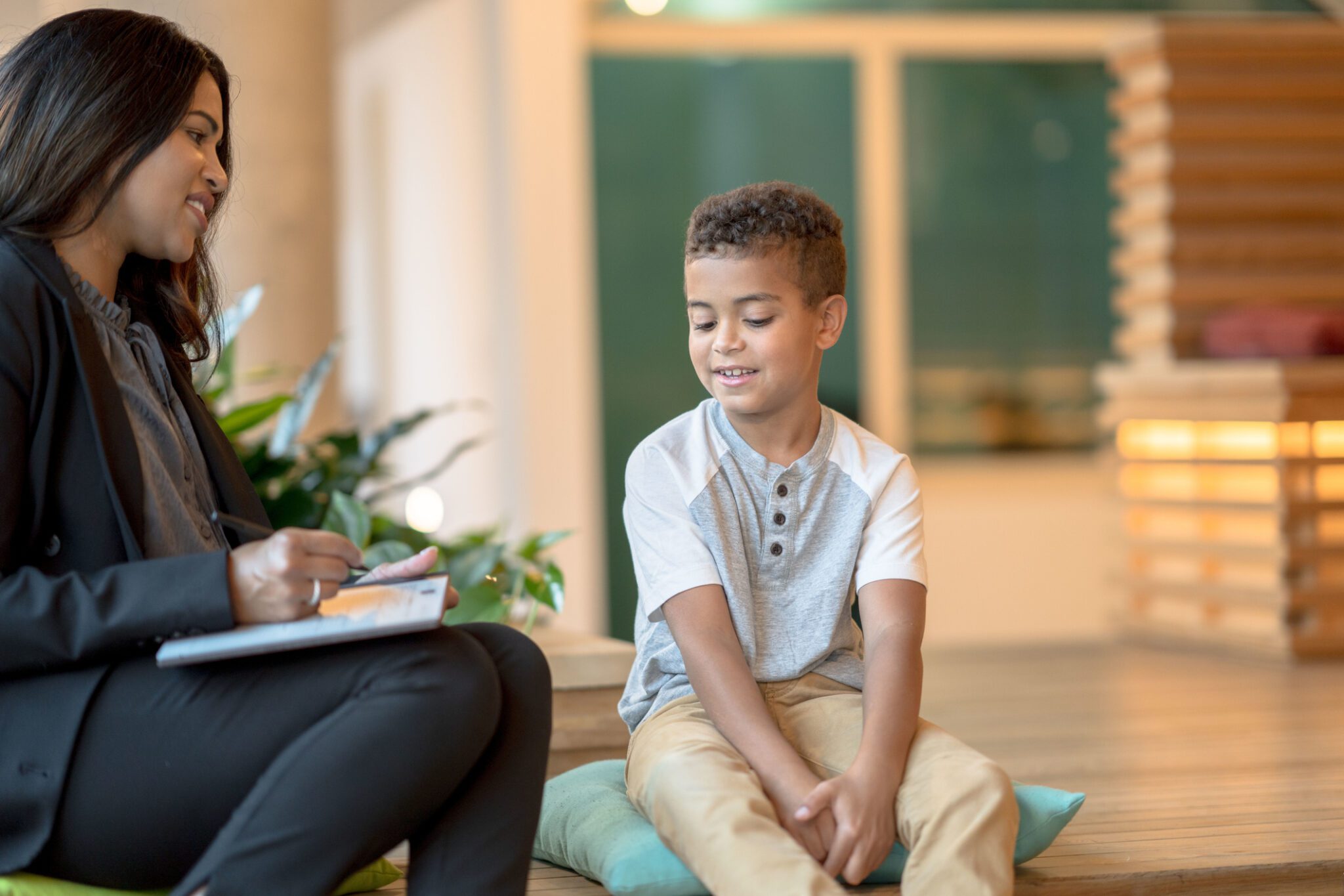 A woman and a boy seated on the floor, both focused on a clipboard in front of them, engaged in an activity together.
