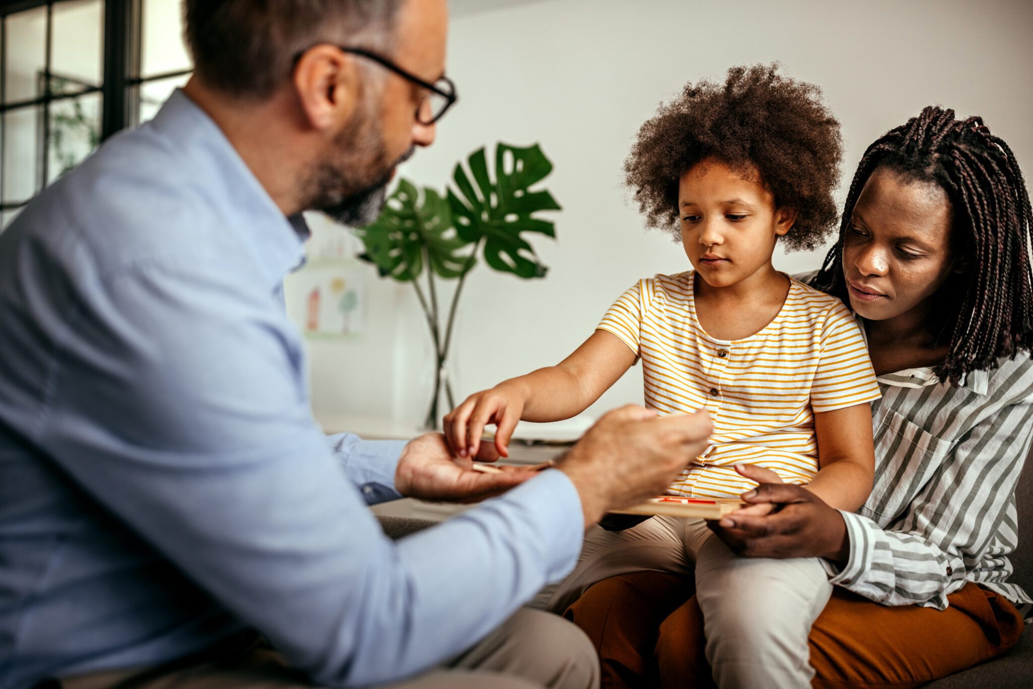 A man and woman sit on a couch, smiling at a child who is playfully nestled between them.