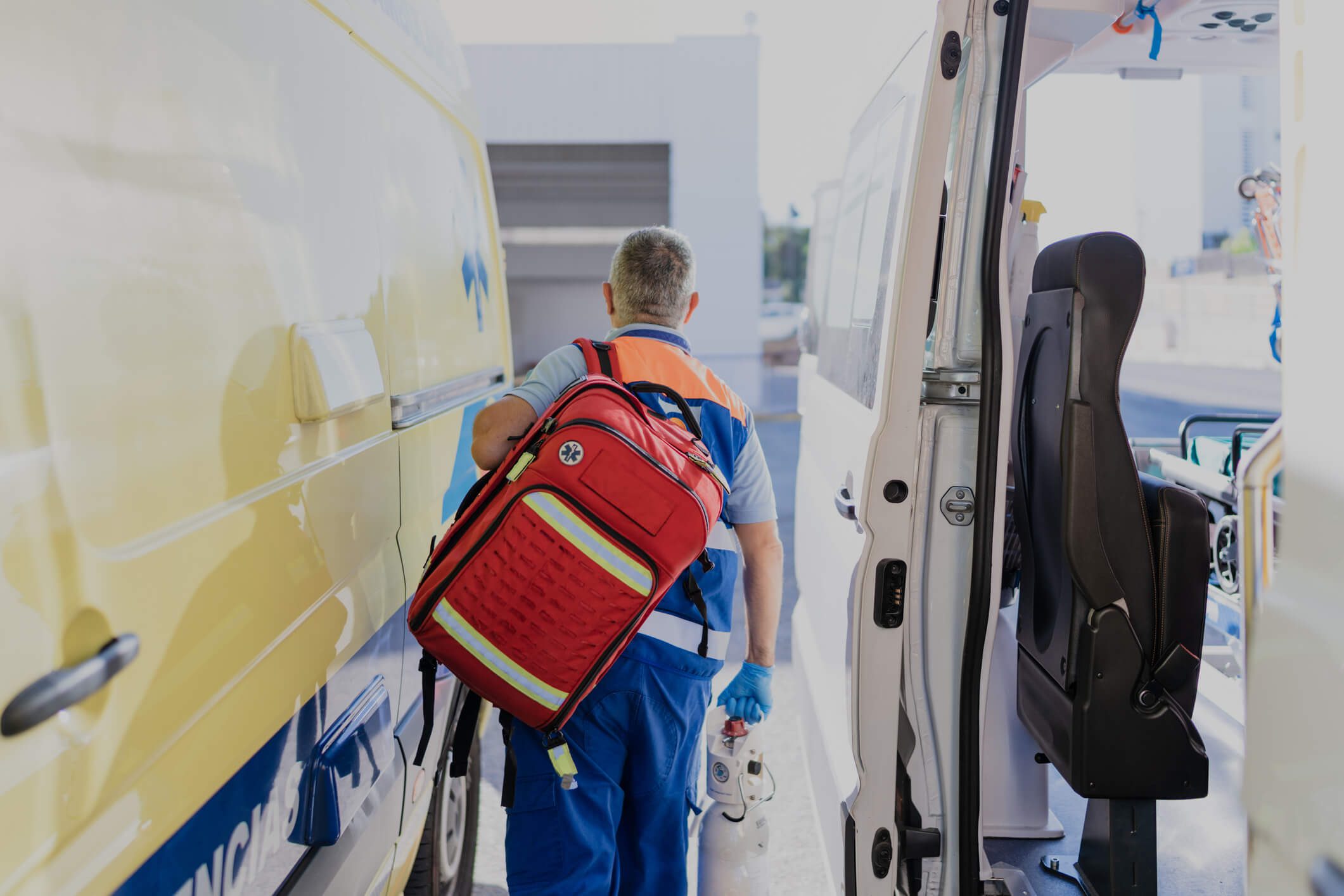 A man in a blue uniform is placing a backpack into the back of a van.