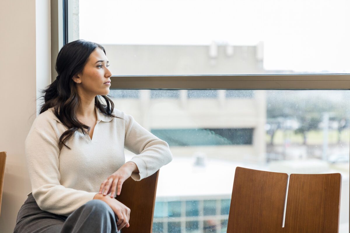 In waiting room, thoughtful young woman looks out window.