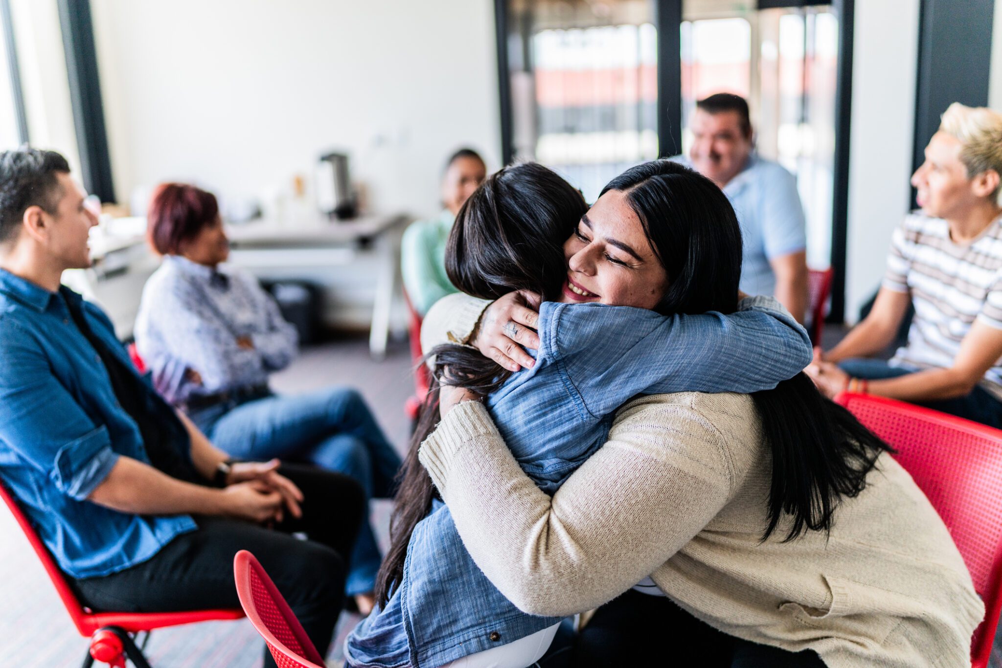 In a meeting room, two women share a heartfelt hug, symbolizing friendship and collaboration.