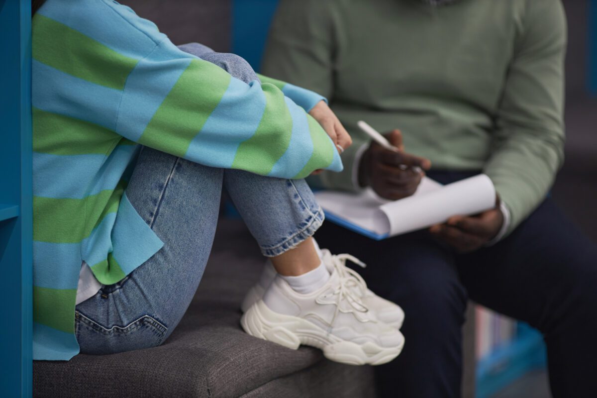Child hugs her knees as a therapist observes and takes notes
